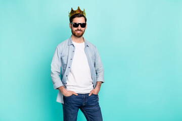 Portrait of positive cheerful man put hands pockets wear golden crown isolated on turquoise color background © deagreez