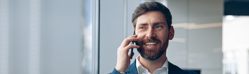 Smiling businessman uses mobile phone to call his business partner while working in the office.