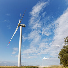 Rotating wind turbines against the cloudy blue sky on sunny summer day