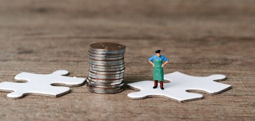 White puzzle pieces and miniature people with business concept. Pile of coins and a miniature man standing on a puzzle.
 - Powered by Adobe
