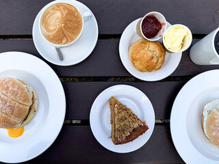 Breakfast in a cafe for two. Directly above. French style breakfast for two in a cafe. Latte art coffee with freshly baked croissant on a black wooden table, Piece of cake, scones, egg and bacon roll.