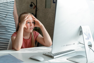 Young shocked tween girl sitting at desk doing homework looking at monitor. Back to school.