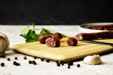 spicy smoked sausages on a cutting board next to red pepper garlic and herbs on a black background