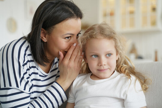 Mother or babysitter whispering sharing secret with kid daughter. Trusting relationship, friendship