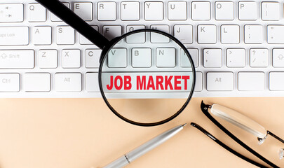 Text JOB MARKET on keyboard with magnifier , glasses and pen on a beige background