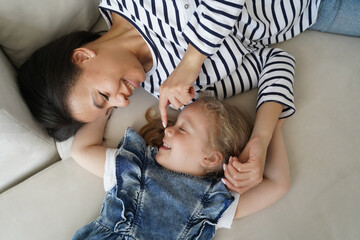 Tenderness to kid. Young mom enjoying morning with her little daughter and relaxing on couch.