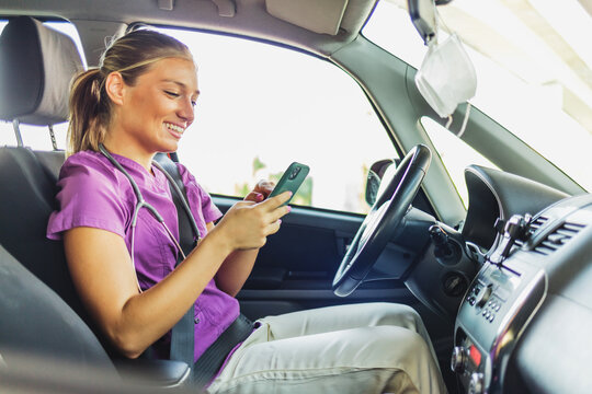 Nurse arriving at a patient's home, she is sitting in her car using her mobile phone. A nurse dressed in her scrubs uniform sitting in her stationary car, holding her mobile phone.