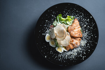 top view of caesar salad with chicken, romaine and egg on black background