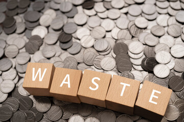 無駄・浪費のイメージ｜「WASTE」と書かれたブロックとコイン
