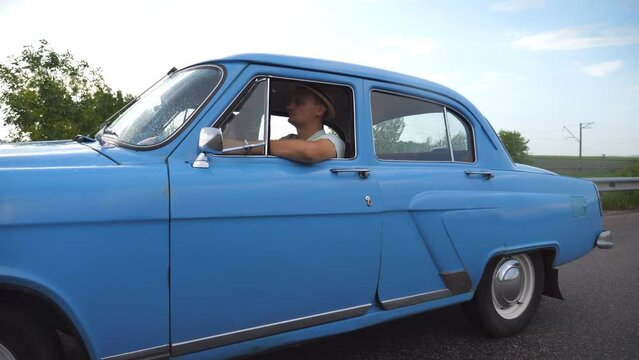 Classic old car traveling on highway on summer day. Young couple driving on country road in vintage automobile. Trip at the retro auto. Concept of summer vacation or holiday. Slow motion Close up