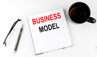 Coffee,glasses,pen and notebook written with BUSINESS MODEL , on white background.