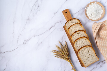 Wheat ears, flour and sliced bread on a light marble table. Top view