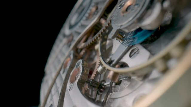 Antique pocket watch mechanism moving on black studio background. Macro shot of clockwork with rotating spring, gears, cogwheel and wheels with tootheds. Disassembled silver retro pocket watch inside.