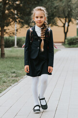back to school. little happy kid pupil schoolgirl eight years old in fashion uniform with backpack...