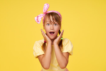 Portrait of surprised cute little toddler girl child over yellow background. Looking at camera....