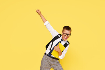 School break. Cheerful mischievous schoolboy in uniform with a backpack jumps on a yellow...