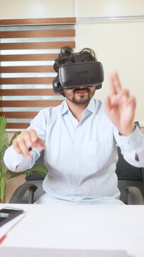 Vertical shot of young businessman busy using VR or virtual reality headset at office with hand gestures - concept of technology, metaverse and futuristic