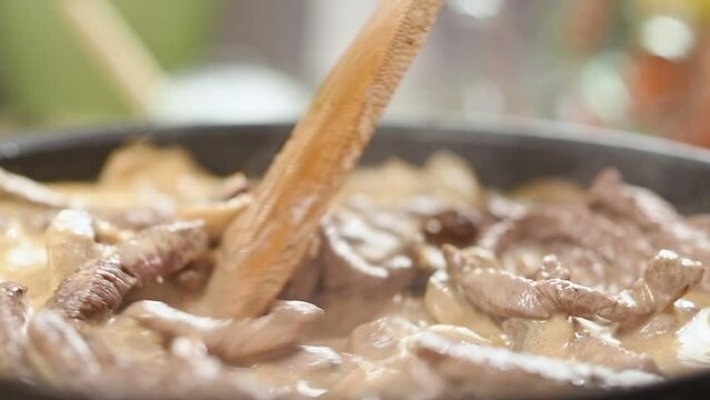 Chef stirring beef stroganoff in a frying pan.

