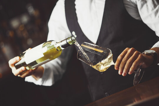 Waiter pours white wine into a glass, close-up.