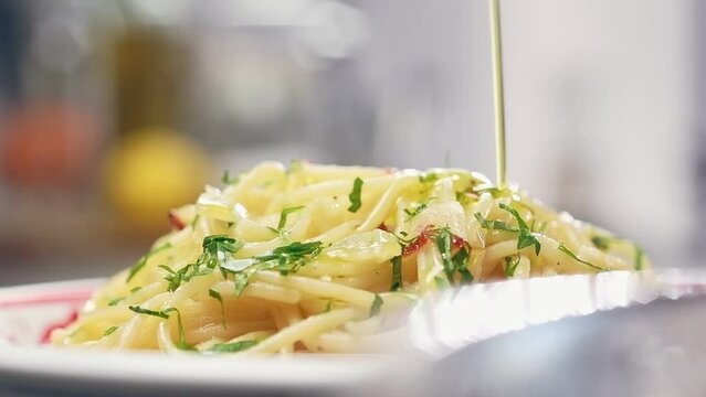 Chef pours olive oil over prepared spaghetti aglio e olio, served on a plate.
