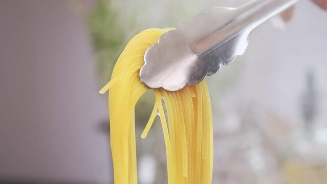 Taking spaghetti with kitchen tongs from saucepan.
