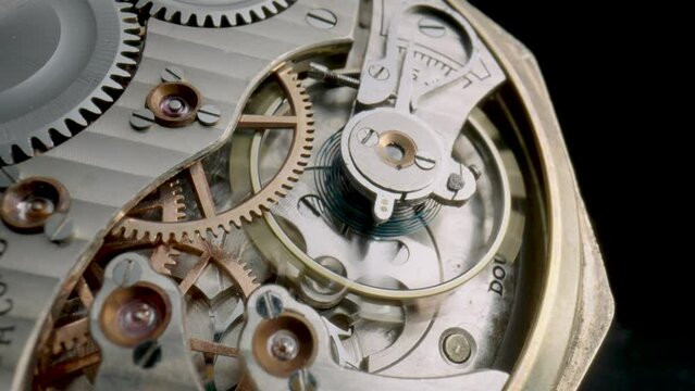 Antique pocket watch mechanism moving on isolated black studio background. Macro shot of clockwork with rotating spring, gears, cogwheel and tootheds wheels. Disassembled silver retro pocket watch.