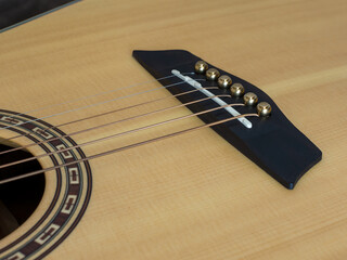 Six-string acoustic guitar with light pine top, polysander bridge and brass pins. Close-up.