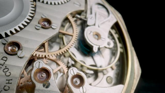 Macro shot of the internal parts of antique pocket watch. Clockwork with rotating spring, gears, cogwheel and wheels with tootheds on isolated black studio background. Disassembled silver watch.