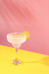 Glass of delicious margarita cocktail isolated over pink yellow background