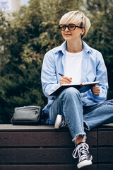 Obraz premium Young woman sitting on bench and writing in a notebook