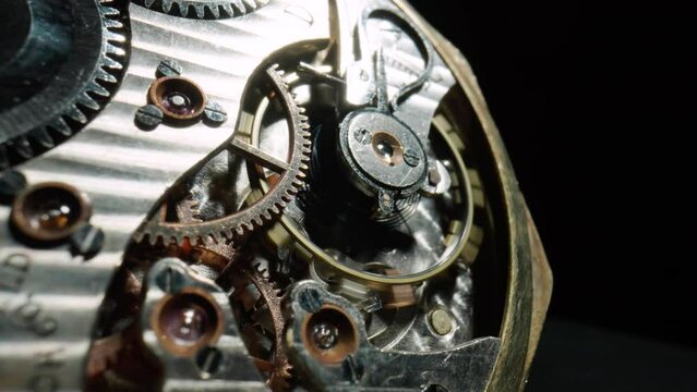 Macro shot of the internal parts of antique pocket watch. Clockwork with rotating spring, gears, cogwheel and wheels with tootheds on isolated black studio background. Disassembled silver retro watch.