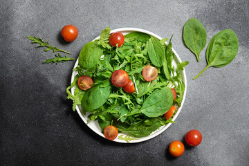 Fresh juicy salad with arugula, baby spinach and cherry tomatoes on dark rustic table top view. Healthy diet food concept.