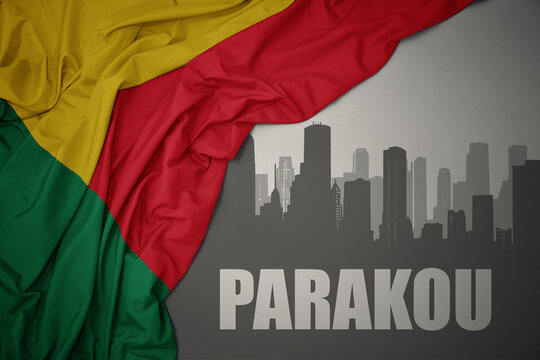 abstract silhouette of the city with text Parakou near waving colorful national flag of benin on a gray background.