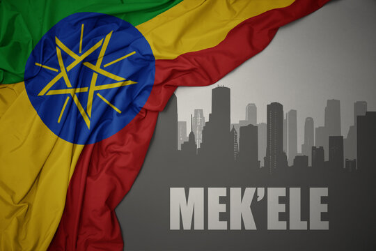 abstract silhouette of the city with text Mek'ele near waving colorful national flag of ethiopia on a gray background.