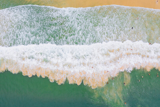 Aerial view of swimmers amongst waves breaking on a sandy beach