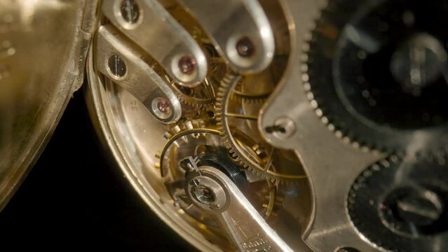 Macro shot of gold internal parts of antique pocket watch. Clockwork with rotating spring, gears, cogwheel and wheels with tootheds on isolated black studio background. Disassembled silver retro watch