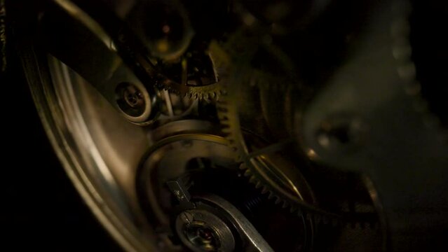 Disassembled gold pocket watch with clockwork turning. Working clock mechanism with rotating spring, gears, gearing and toothed wheels. Macro shot moving clockwork that appear and disappear in dark