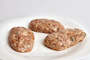 Raw cutlets from minced meat on a white plate.