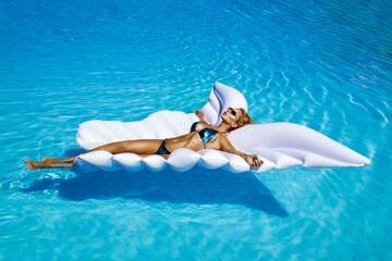 Elegant female model in stylish bikini is lying on a butterfly-shaped mattress in the pool. Sexy woman in amazing sequin bikini is posing in the pool on Maldives island. Vogue. Bikini fashion.