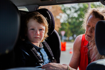Kid being clicked into child booster seat in car by grandmother