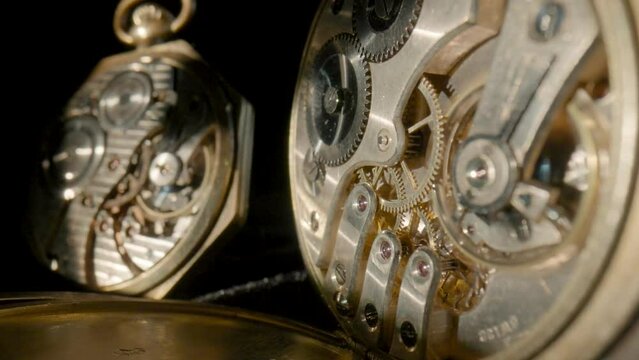 Two antique pocket watches with working clockwork on isolated black studio background. Close up moving gears inside old mechanic pocket watch. Working clock mechanism with rotating spring and gears.