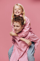 cute, joyful children play and the boy rolls his sister on his back in pink clothes on a pink background. Themes of relationships and friendship between children