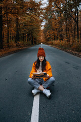 Confidence woman with book sitting on the road with autumn tree around. New life, path choice, ambition