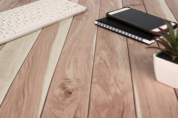 Cellphone, note book, potted plant and white keyboard on wooden desk.