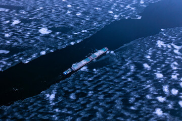A cargo container ship moves along a frozen river. Freight transportation concept, import export and business logistics, aerial view in winter.