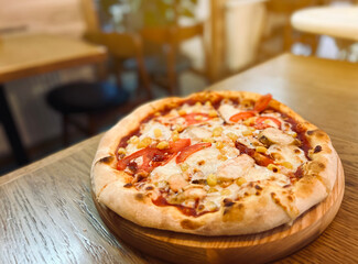 Pizza with chicken, tomatoes, corn and mozzarella is on the table in a plate. Restaurant food. selective focus