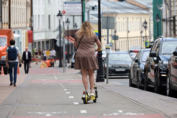 Woman in summer dress ride electric scooter on a street. Travel and leisure in summer city