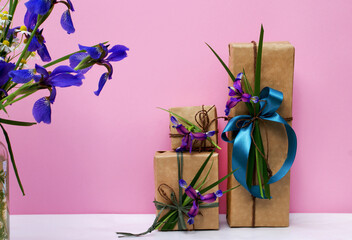 Gifts in craft paper with iris flowers on a pink background