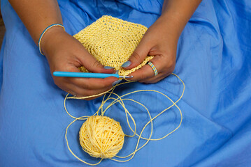 Crocheting yellow raffia against a blue dress