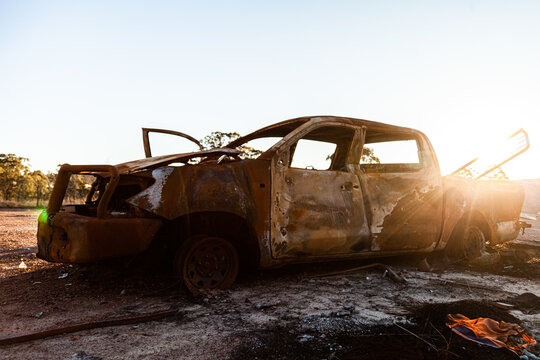 Smashed up burnt out cars on gravel patch backlit by sunflare